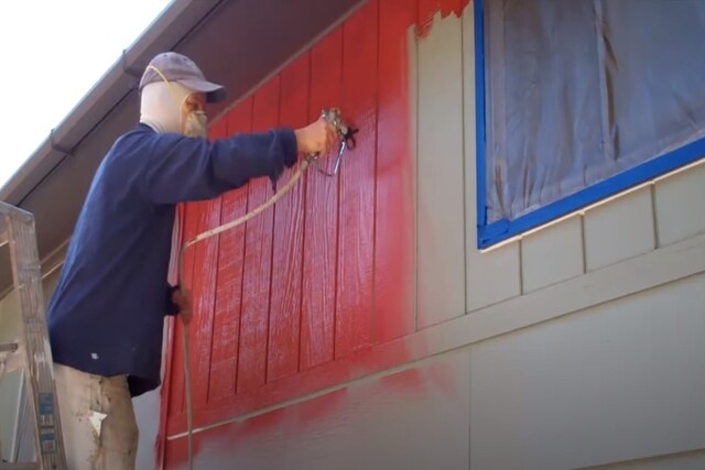 Exterior house spray painting by worker with a mask on