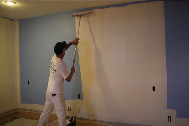 Interior painting by worker with pole and big paint brush