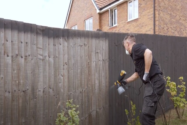 Worker spray painting backyard fence with spray gun