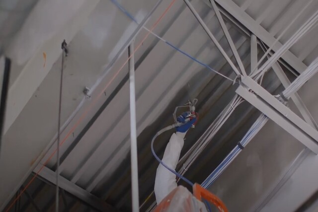 Painting a commercial building interior ceiling with a spray gun