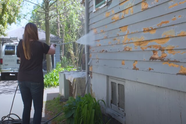 Worker spraying the house wall with water to remove old paint to prep it for a new coat